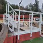 Garde-corps PRV blanc sur passerelle devant un bâtiment à bardage rouge